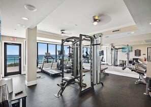 Une salle de sport équipée de machines de cardio, de matériel de musculation et offrant une vue sur l’océan grâce à de grandes fenêtres.