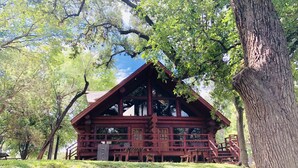 A rustic cabin with a sloped roof, wooden exterior, and a porch with benches. - Waterfront Cabin w/ Stunning Lake Views & Porch (Burnet)