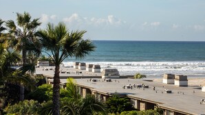 Una terraza en la azotea con vista al océano, palmeras y una playa.