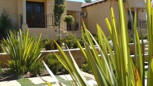 A residential building with a beige facade, numbered 16 and 14, featuring a balcony with a wrought iron railing and a small tree. - The Moon and Sixpence Garden Guest House (Muldersdrift)