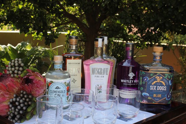 Varias botellas de ginebra y vasos para chupitos sobre una mesa con un arreglo floral.