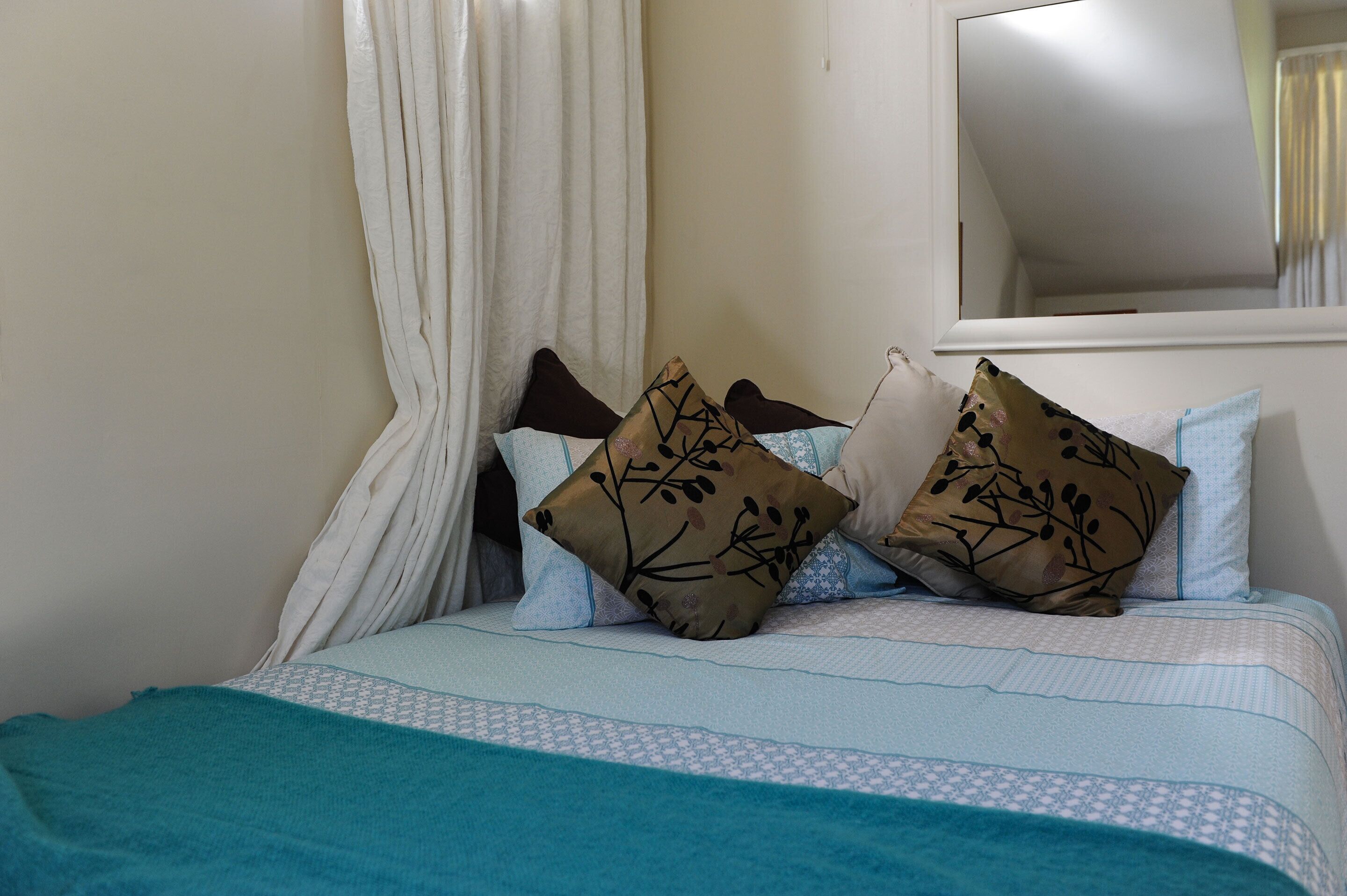 Una cama con manta color turquesa, ropa de cama blanca y azul, y almohadas decorativas.