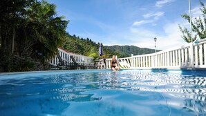 A swimming pool with a person sitting on the edge, surrounded by a white fence and lush greenery. - Tirimoana House (Anakiwa)