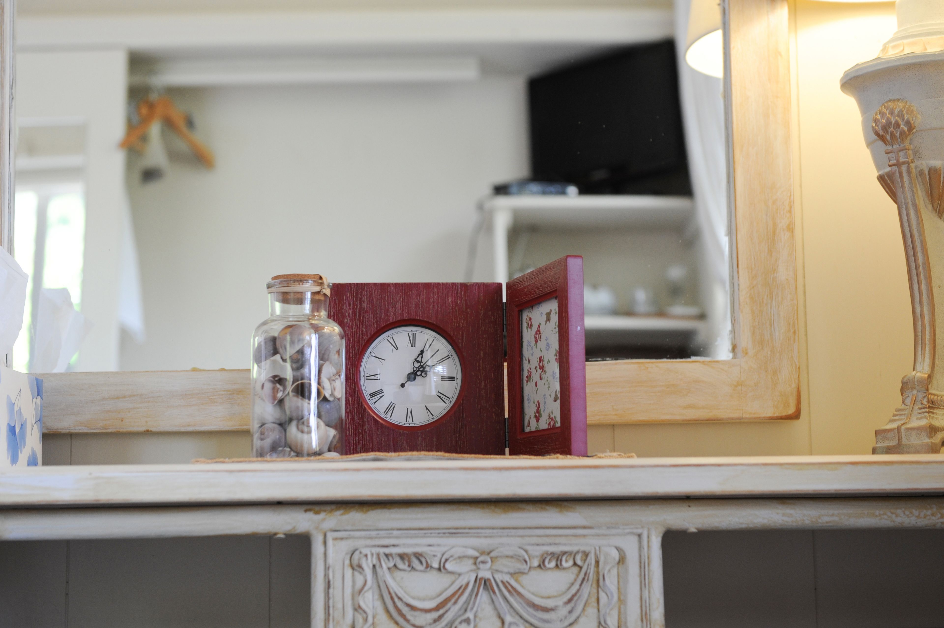 Un reloj sobre una repisa con un espejo que refleja una habitación.