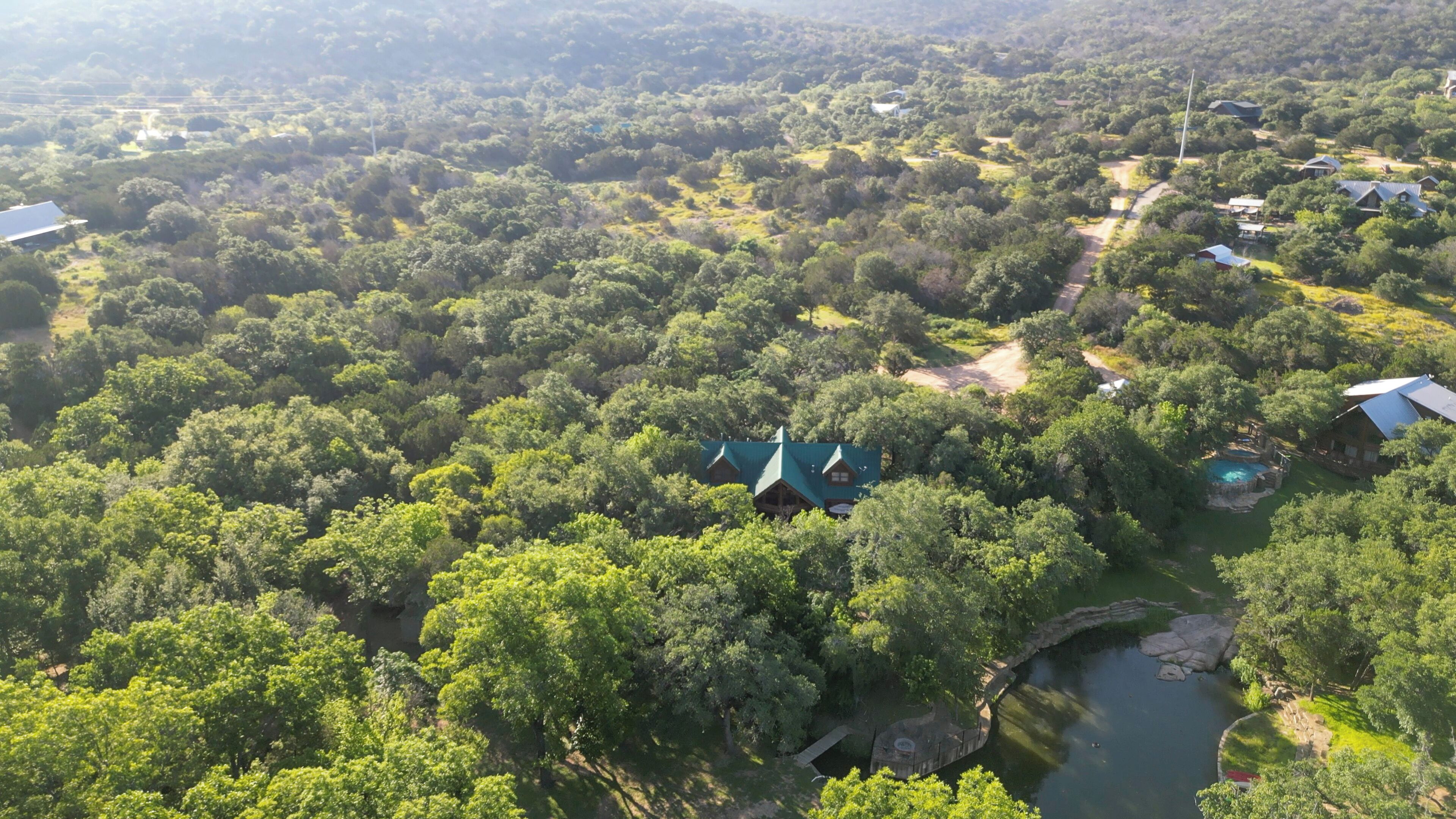Luchtbeeld van een resort met meerdere gebouwen, omgeven door dicht bos, een zwembad en een kleine waterpartij.