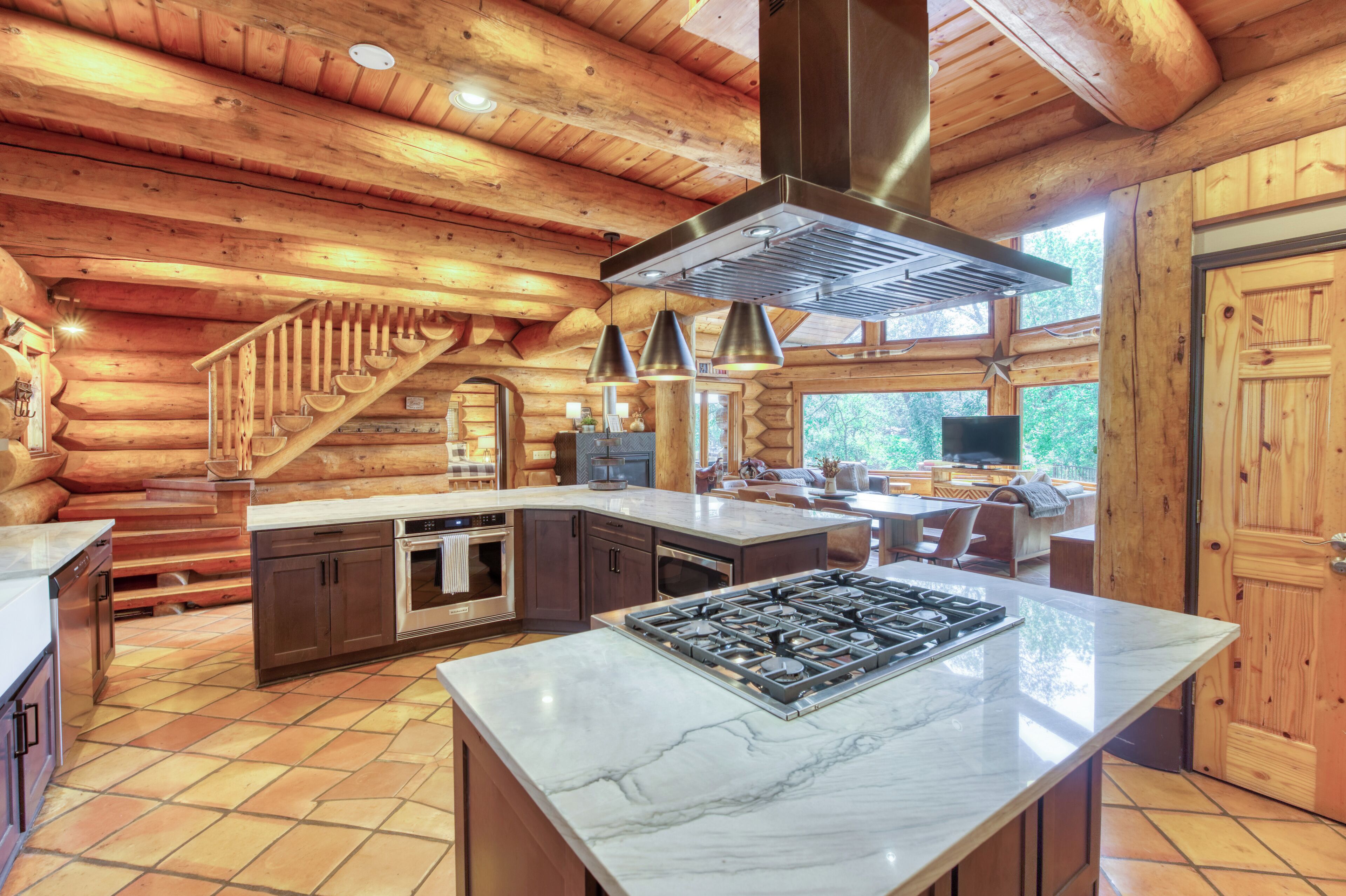 A log cabin interior with a kitchen featuring marble countertops, a gas stove, and a large island.