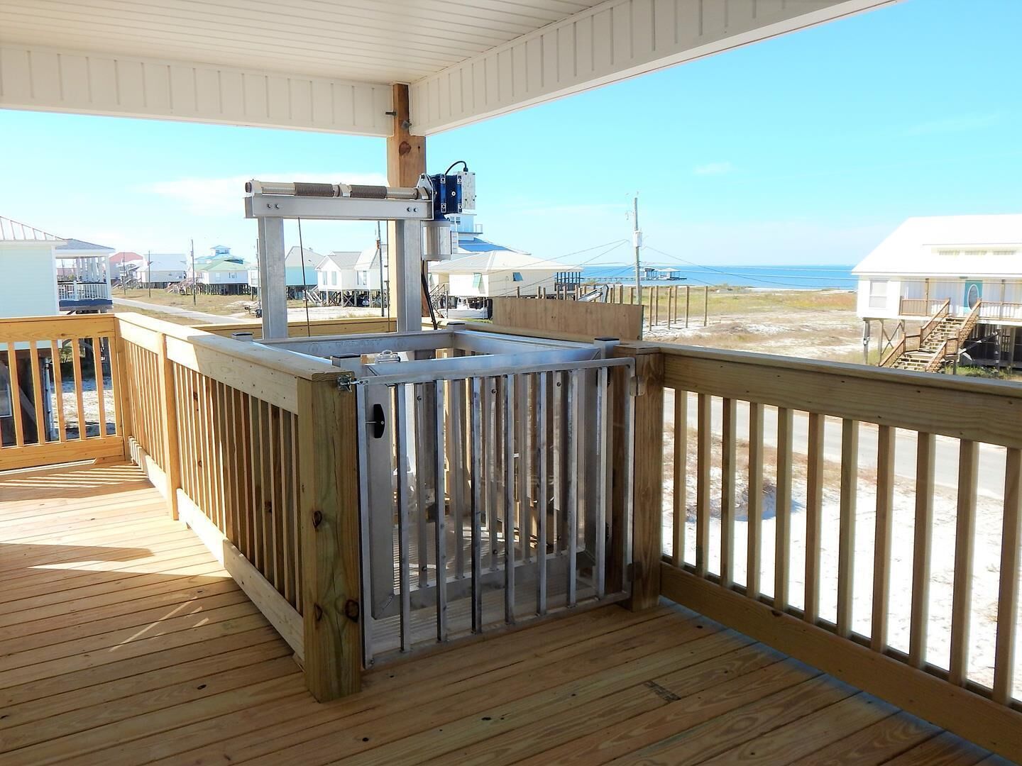 Eine Holzterrasse mit einem Metallzaun, mit Blick auf einen Strand mit Strandhäusern.