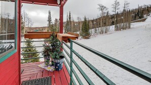 A wooden deck with a red railing, potted plants, and a view of a snowy landscape with trees. - Fireplace | Giant Steps Condo | Ski Out Access (Brian Head)