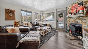 A living room with a sectional sofa, a fireplace, and large windows. - Fireplace | Giant Steps Condo | Ski Out Access (Brian Head)