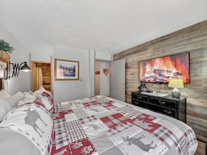 A bedroom with a large bed, a TV displaying a fireplace, and a wooden wall. - Giant Steps 12 Rustic Retreat ski in/out 2bd/2bath (Brian Head)