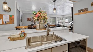 A kitchen with a stainless steel sink, a vase of flowers, and a wooden bench. - Fireplace | Giant Steps Condo | Ski Out Access (Brian Head)