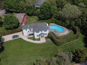 Une vue aérienne d’une maison avec une piscine, entourée de pelouses et d’arbres bien entretenus.