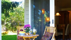 A wooden table with a bowl of fruit, a bottle, and a glass of wine on a balcony with wicker chairs and a cushion. - Jackson Hole Condo, 5 Miles from Grand Teton National Park,4 miles to ski resort (Wilson)