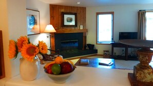 A living room with a fireplace, a bowl of fruit, and a vase of sunflowers. - Jackson Hole Condo, 5 Miles from Grand Teton National Park,4 miles to ski resort (Wilson)