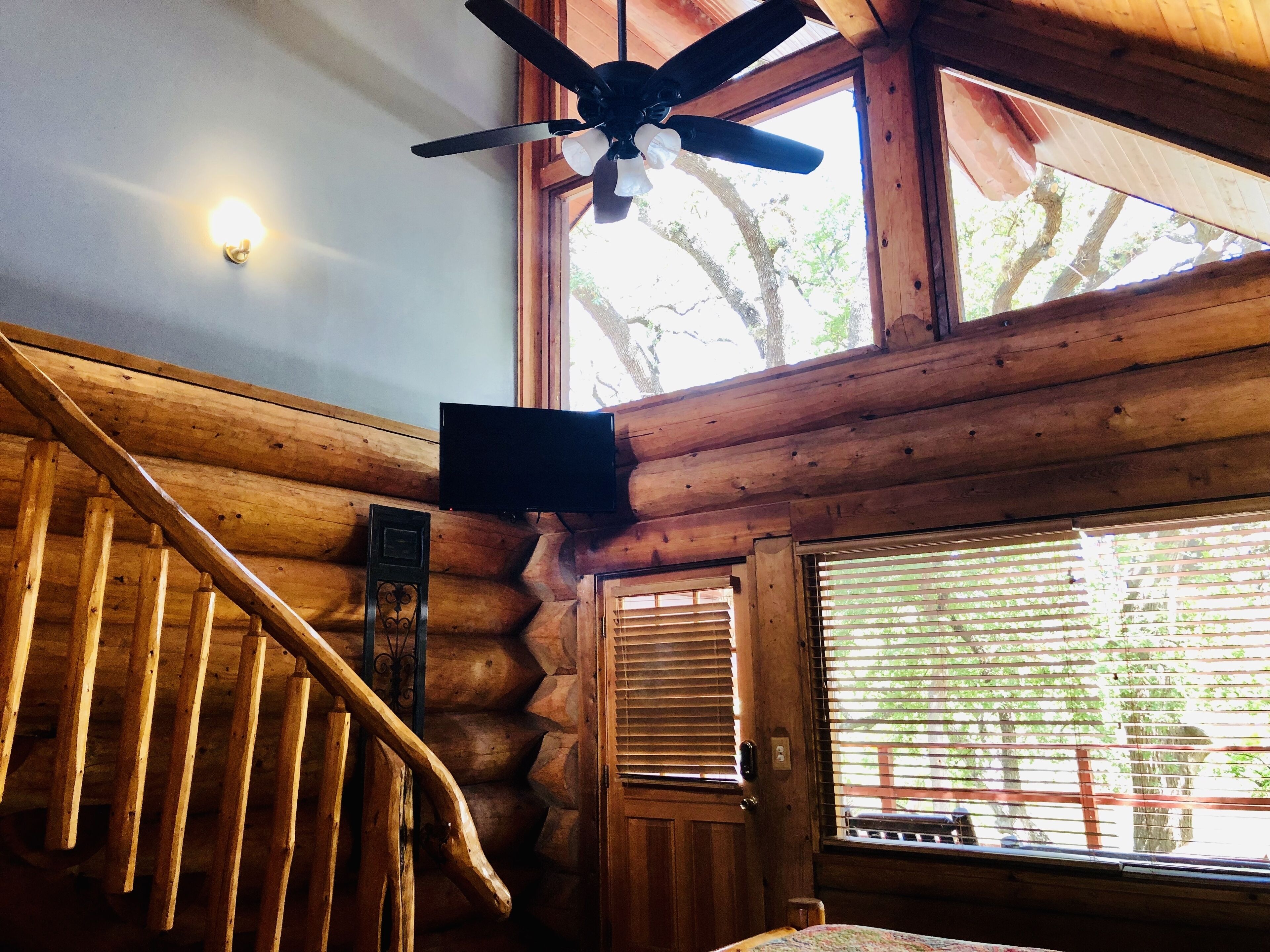 L’intérieur d’une cabane en bois est doté d’un escalier, d’un ventilateur de plafond, d’une télévision et d’une grande fenêtre avec des stores.
