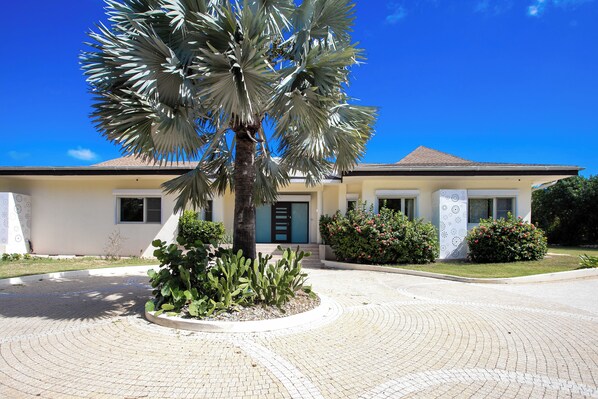 Un edificio moderno con una entrada curva, una palmera y jardines bien cuidados.