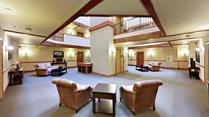 Eine geräumige, mehrstöckige Hotelhalle mit hoher Decke, Holzbalken und einer zentralen Treppe.