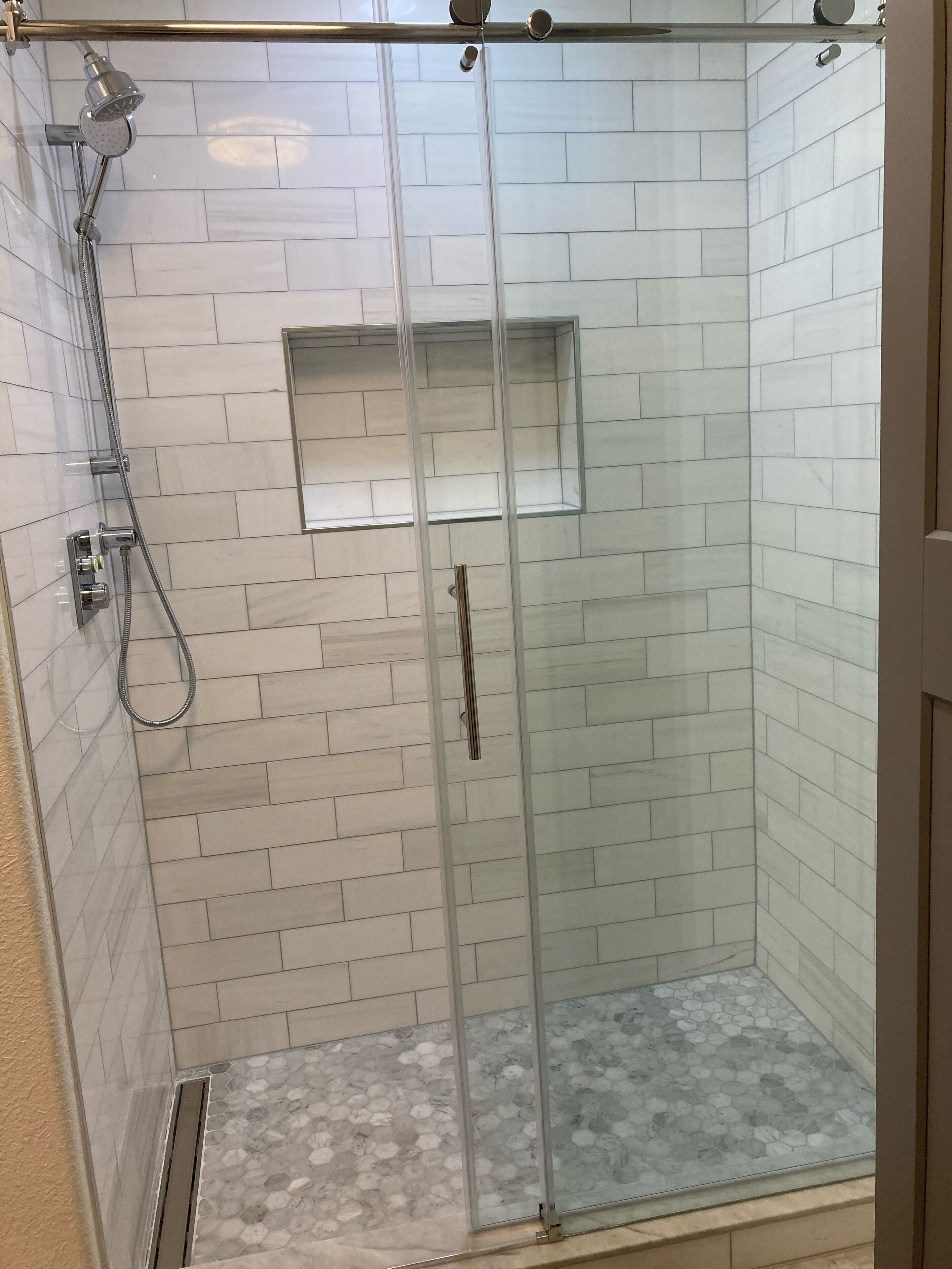 A glass-enclosed shower with a tiled wall, a built-in shelf, and a showerhead.