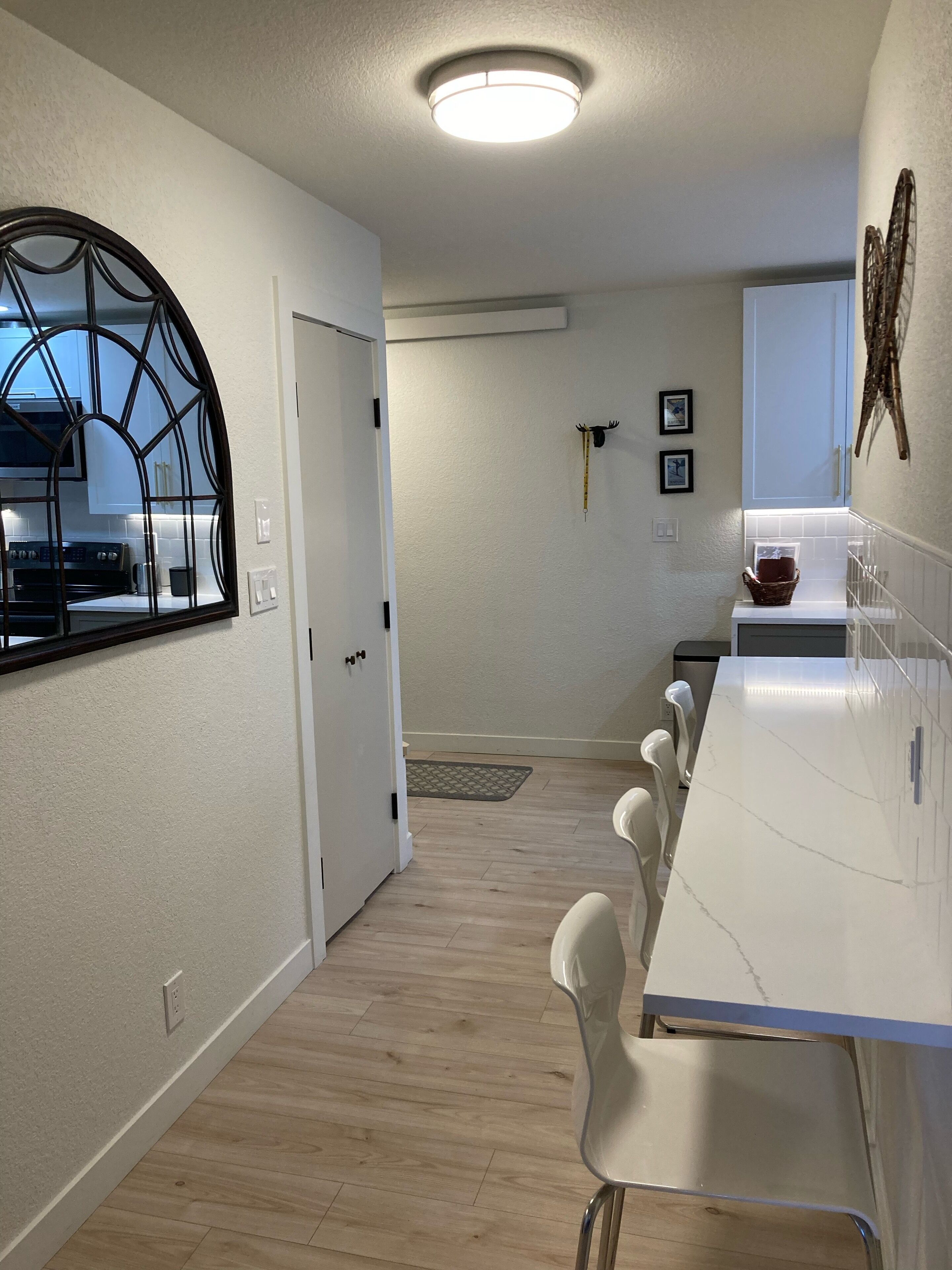 A modern kitchen with a white countertop, a large window, and a dining area with white chairs.
