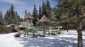 Ein Spielplatz mit einer Wendelrutsche und Klettergerüsten, umgeben von Schnee und Bäumen.