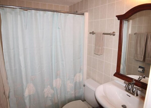 A bathroom with a shower curtain, a toilet, a sink, and a mirror. - STBT 117: Seaside Escape: Pool & Beach Access (St. Augustine)