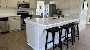 Une cuisine moderne avec des meubles blancs, des appareils en acier inoxydable et un grand îlot central doté de tabourets.
