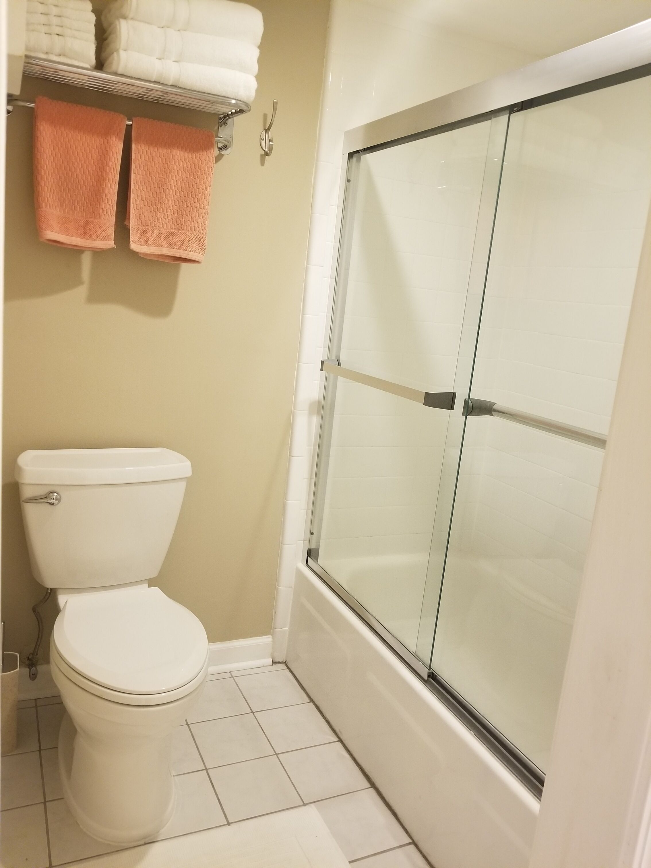 A bathroom with a toilet, a glass-enclosed shower, and a towel rack with folded towels.