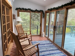 A wooden chair and a table lamp in a sunlit room with a view of a deck and trees. - Family get away to this charming cottage on 600 ft of Lake (East Springfield)