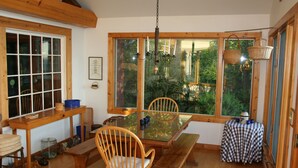 Un coin repas avec une table en bois, des chaises et un banc. Une fenêtre offre une vue sur la verdure à l’extérieur.