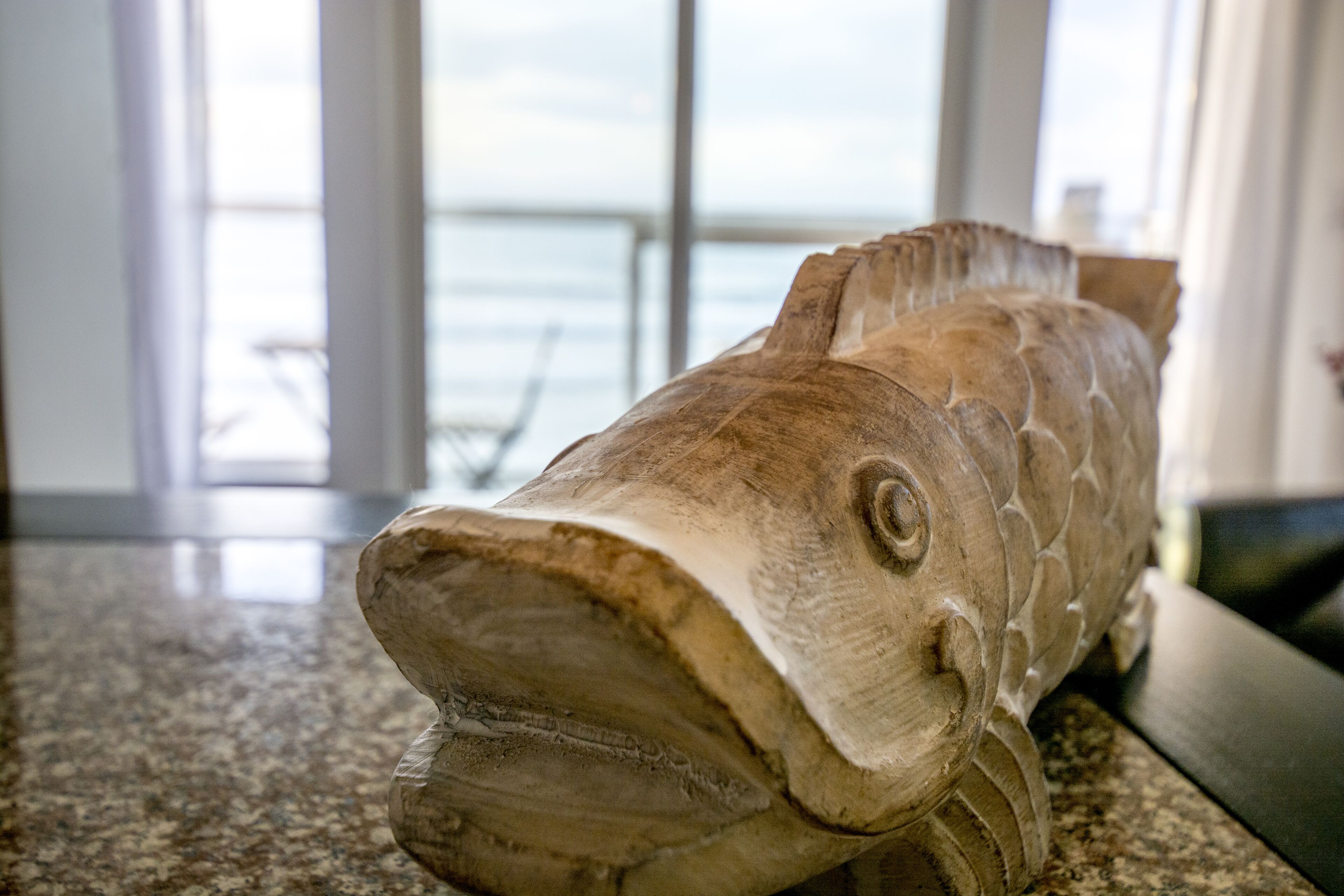 En träskulptur i form av en fisk, placerad på en bänkskiva av granit.