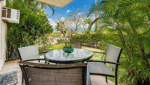 Un patio con una mesa redonda de vidrio y cuatro sillas, rodeado de abundante vegetación y vistas a una zona residencial.