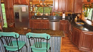 A kitchen with wooden cabinets, a stainless steel refrigerator, a dishwasher, and a granite countertop. - Lakefront•3BR/3.5BA+Loft•Hot Tub&Boat House (Burnet)