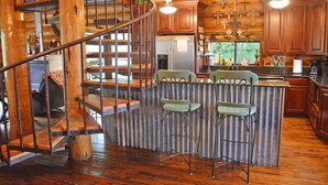 A rustic kitchen with wooden cabinets, a stainless steel refrigerator, and a bar area with two bar stools. - Lakefront•3BR/3.5BA+Loft•Hot Tub&Boat House (Burnet)
