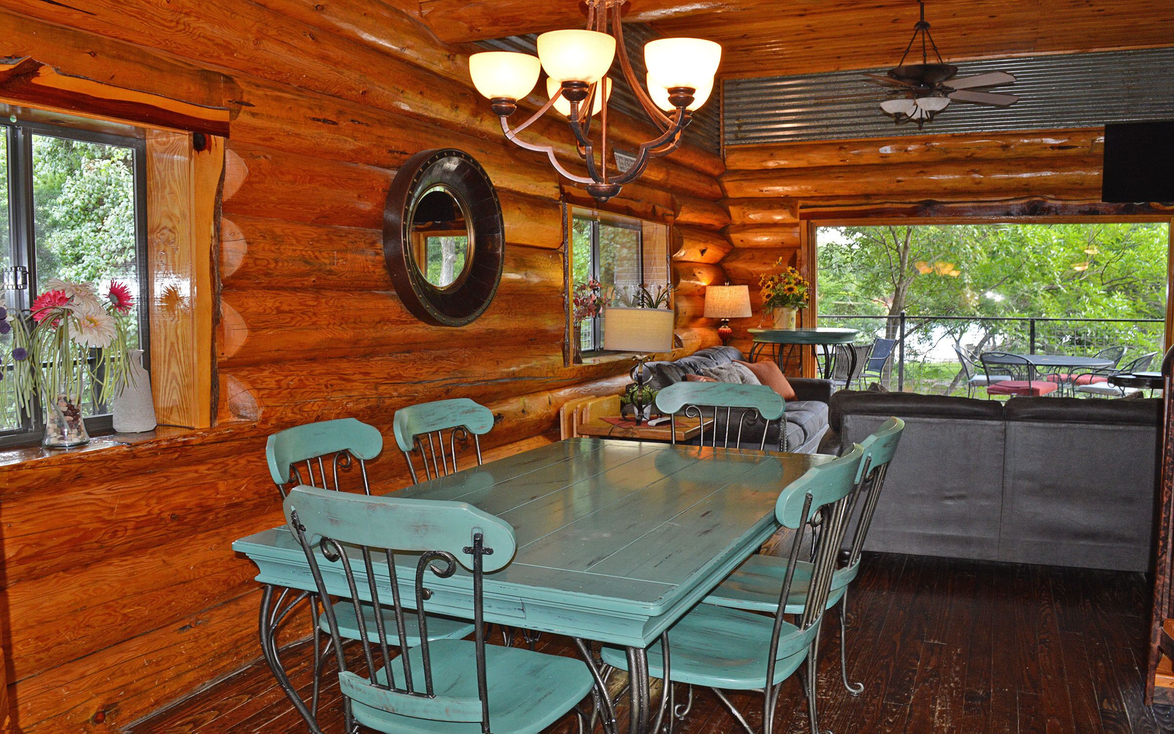 A rustic cabin interior with a dining area, a sofa, and a view of the outdoors.
