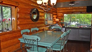 A rustic cabin interior with a dining area, a sofa, and a view of the outdoors. - Lakefront•3BR/3.5BA+Loft•Hot Tub&Boat House (Burnet)