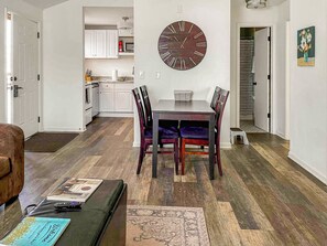 A dining area with a wooden table and chairs, a large wall clock, and a kitchen in the background. - 2 BR Retreat - 8 Min to Broadway - Free Parking - Close to Everything  - A (Nashville)