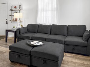 A modern living room with a grey sectional sofa, a small side table, and a magazine on a round ottoman.