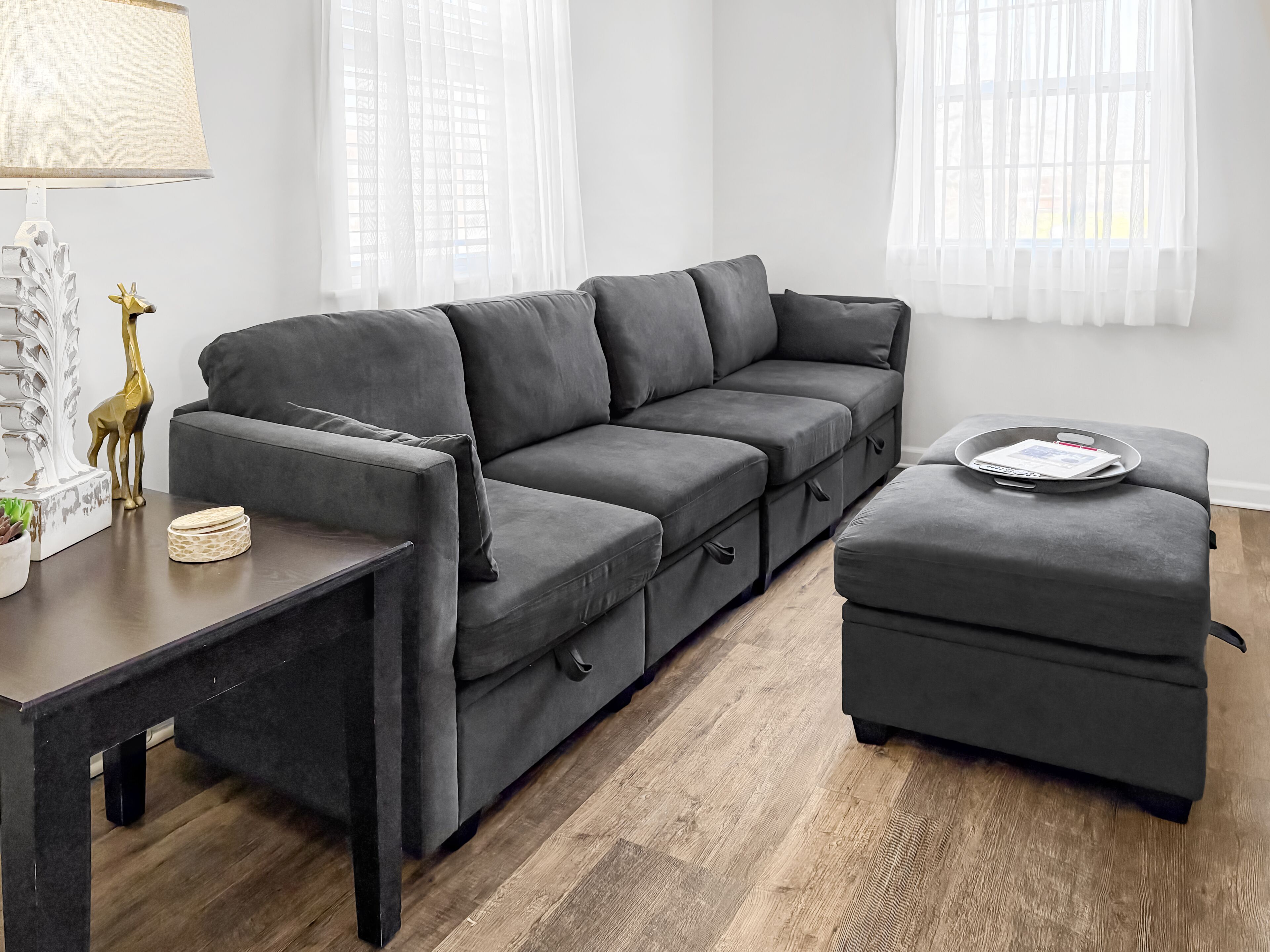 A modern living room with a grey sectional sofa, a small ottoman, and a side table with decorative items.