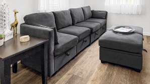 Een moderne woonkamer met een grijze modulaire bank, een klein voetenbankje en een bijzettafeltje met decoratieve objecten.