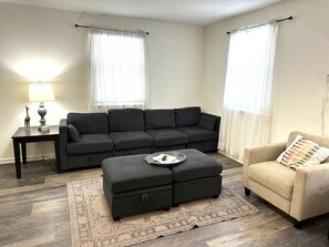 A living room with a sofa, ottoman, and armchair, a side table, and a lamp. - 2 BR - 8 Min to Broadway - Free Parking - A (Nashville)