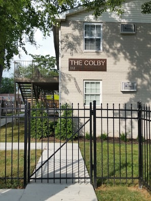 Welcome to The Colby, a charming two-story building with a brick facade and inviting porch area.