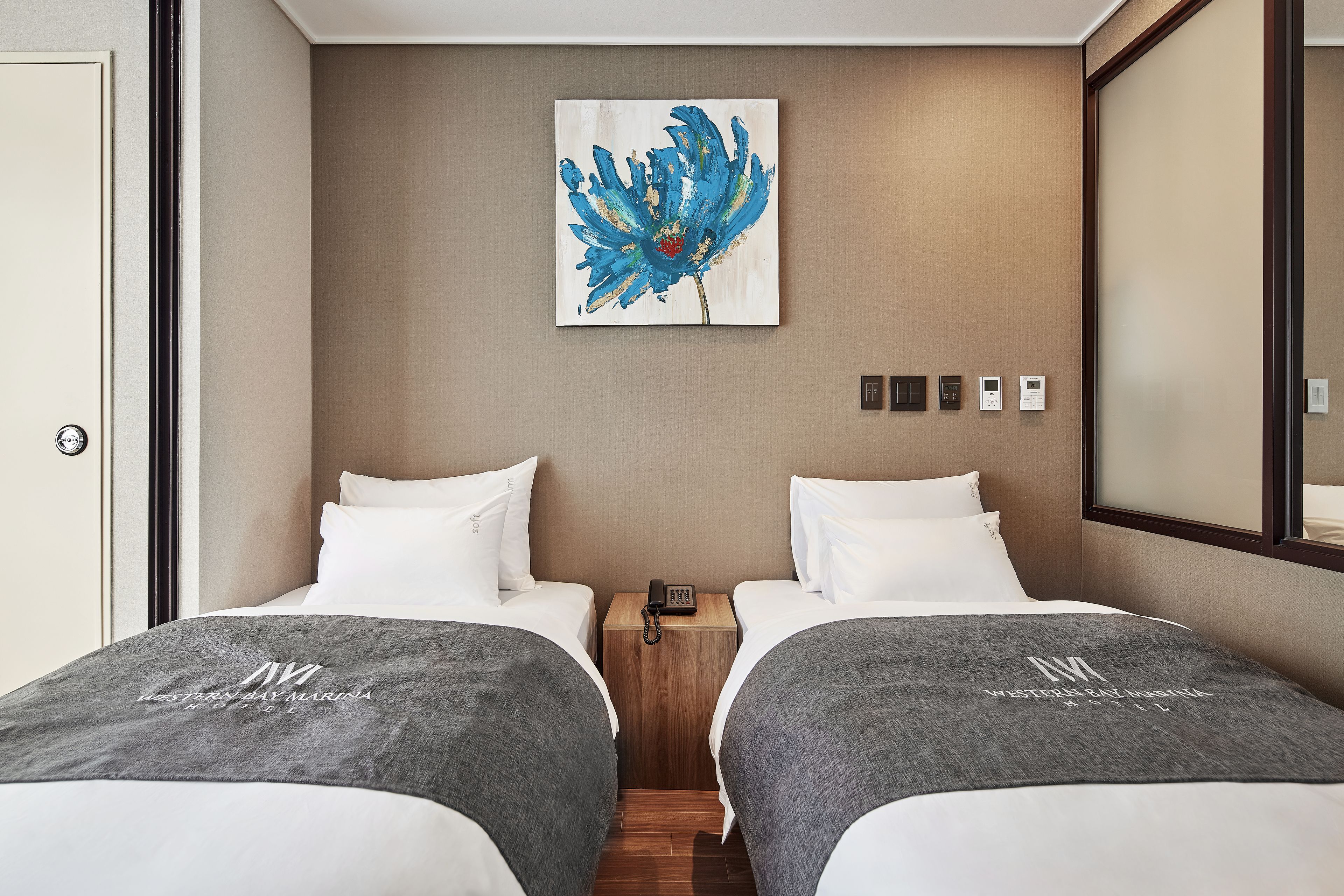 A hotel room with two beds, a nightstand with a phone, a painting on the wall, and a mirror.
