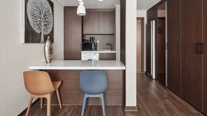 Een moderne keuken met een centraal eiland, twee barkrukken, een hanglamp en een grote kunstwerk van een boom aan de muur.