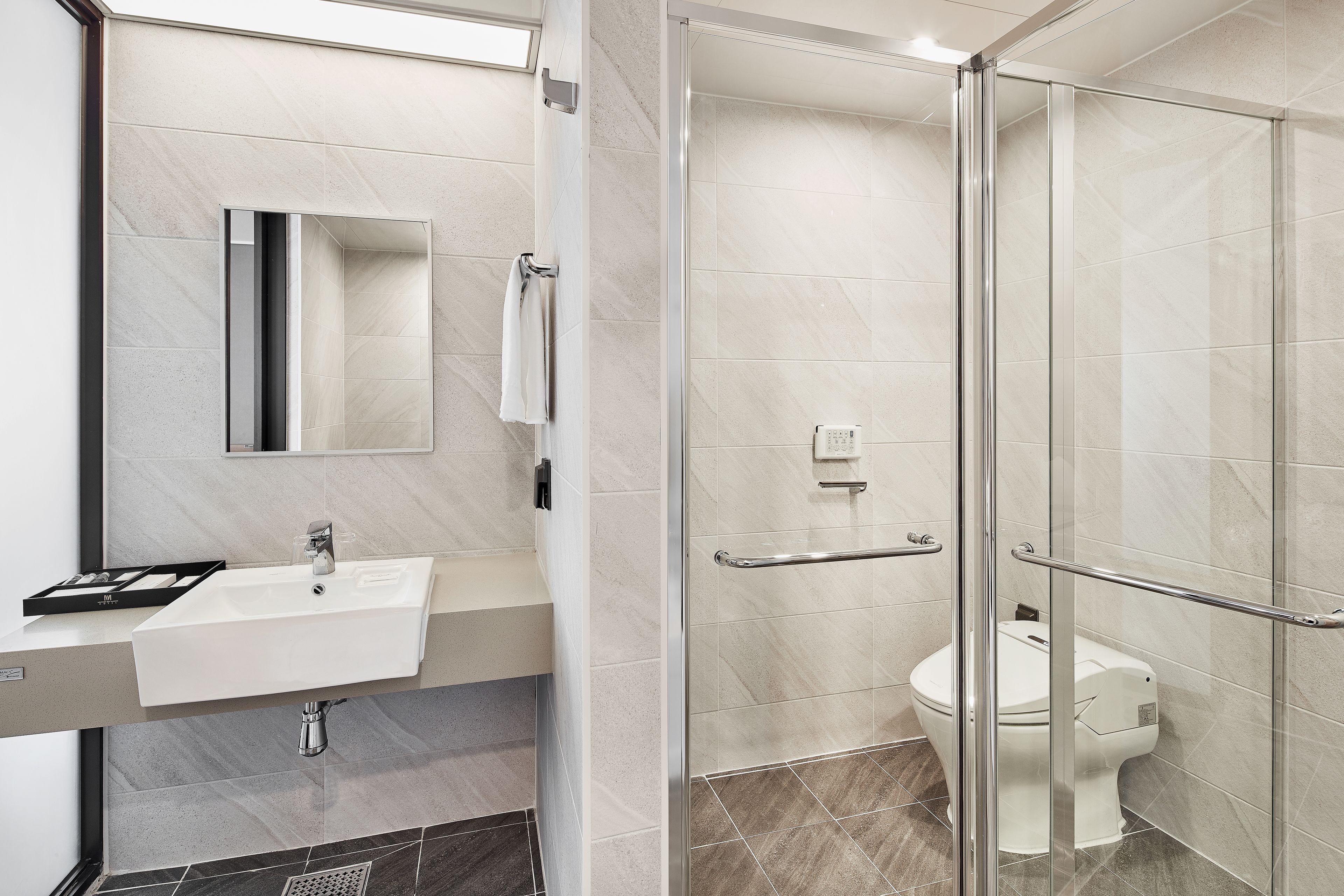 Et moderne badeværelse med et glasbrusekabine, en hvid vask og et toilet.