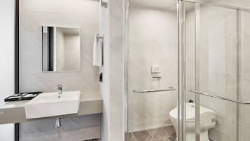 Et moderne badeværelse med et glasbrusekabine, en hvid vask og et toilet.