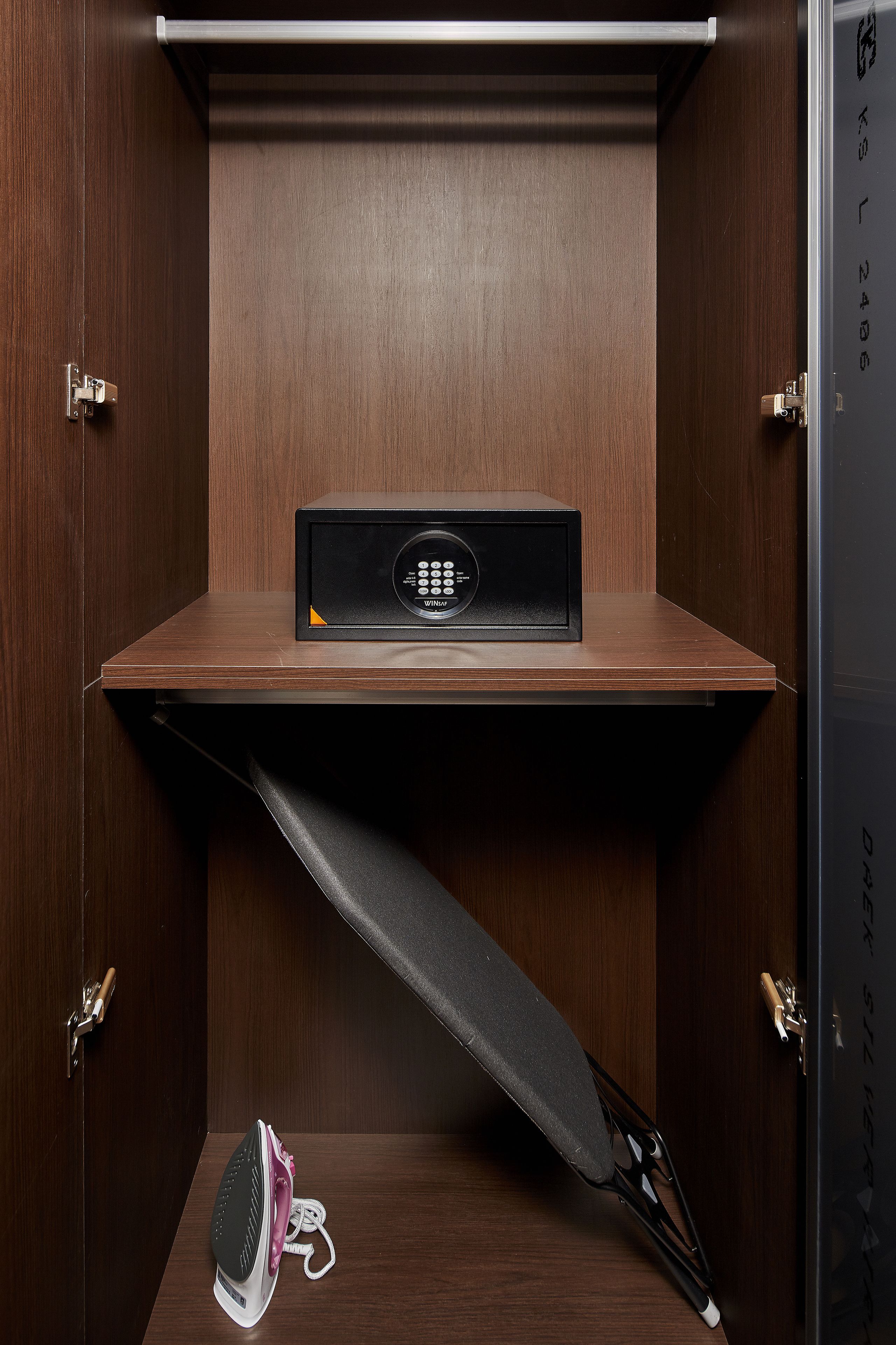 A compact, dark wooden room with a built-in ironing station, including an iron, board, and a small black appliance, likely a microwave or coffee maker.