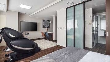 Ett modernt hotellrum med en massagefåtölj, en platt-TV, ett skrivbord med stol och en skjutdörr i glas som leder till badrummet.