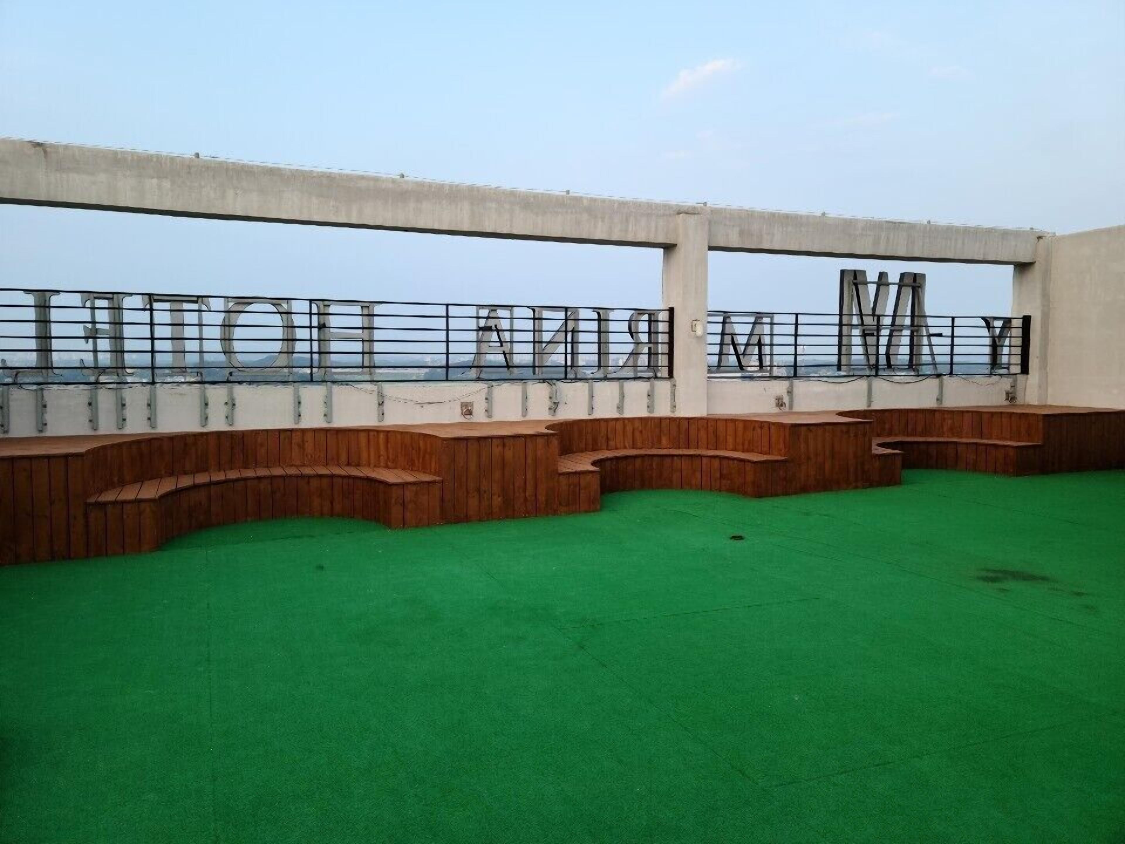 A rooftop terrace with a green floor, wooden seating, and a metal railing with large letters spelling "HELLO WORLD".