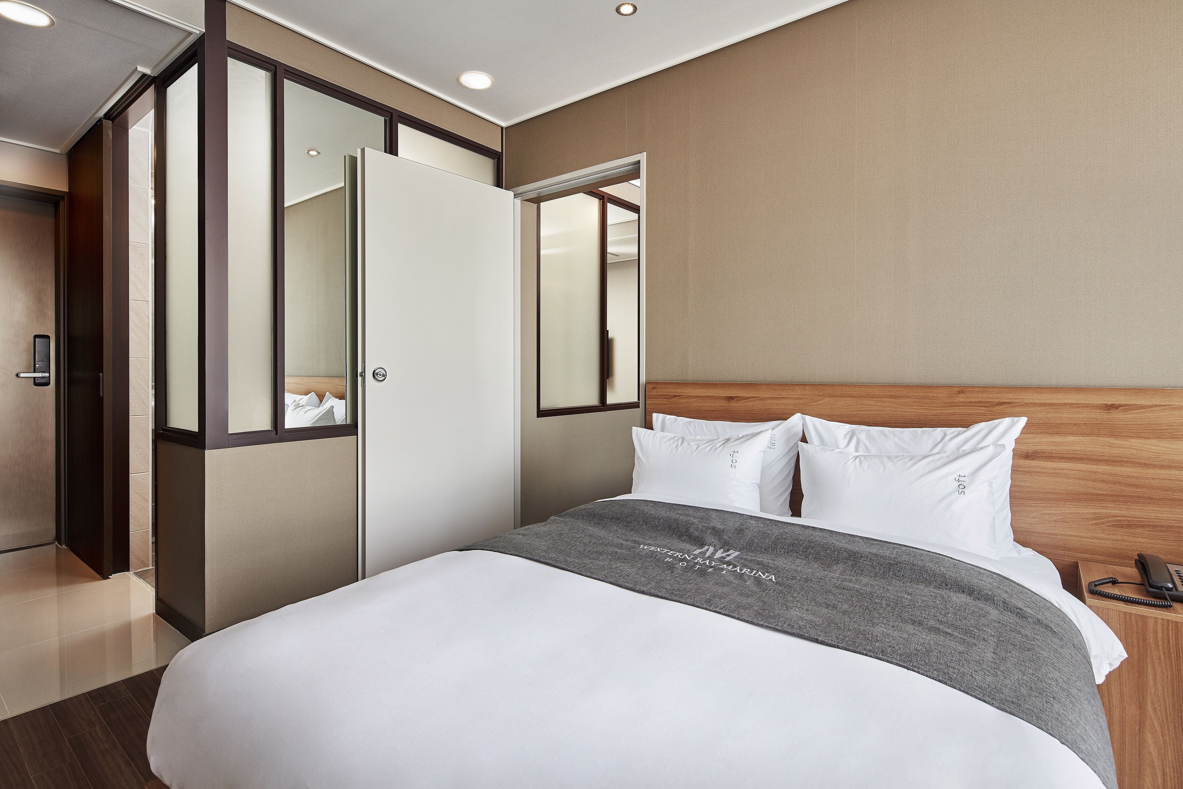 A hotel room with a large bed, a wooden headboard, a grey blanket, and a bedside telephone.