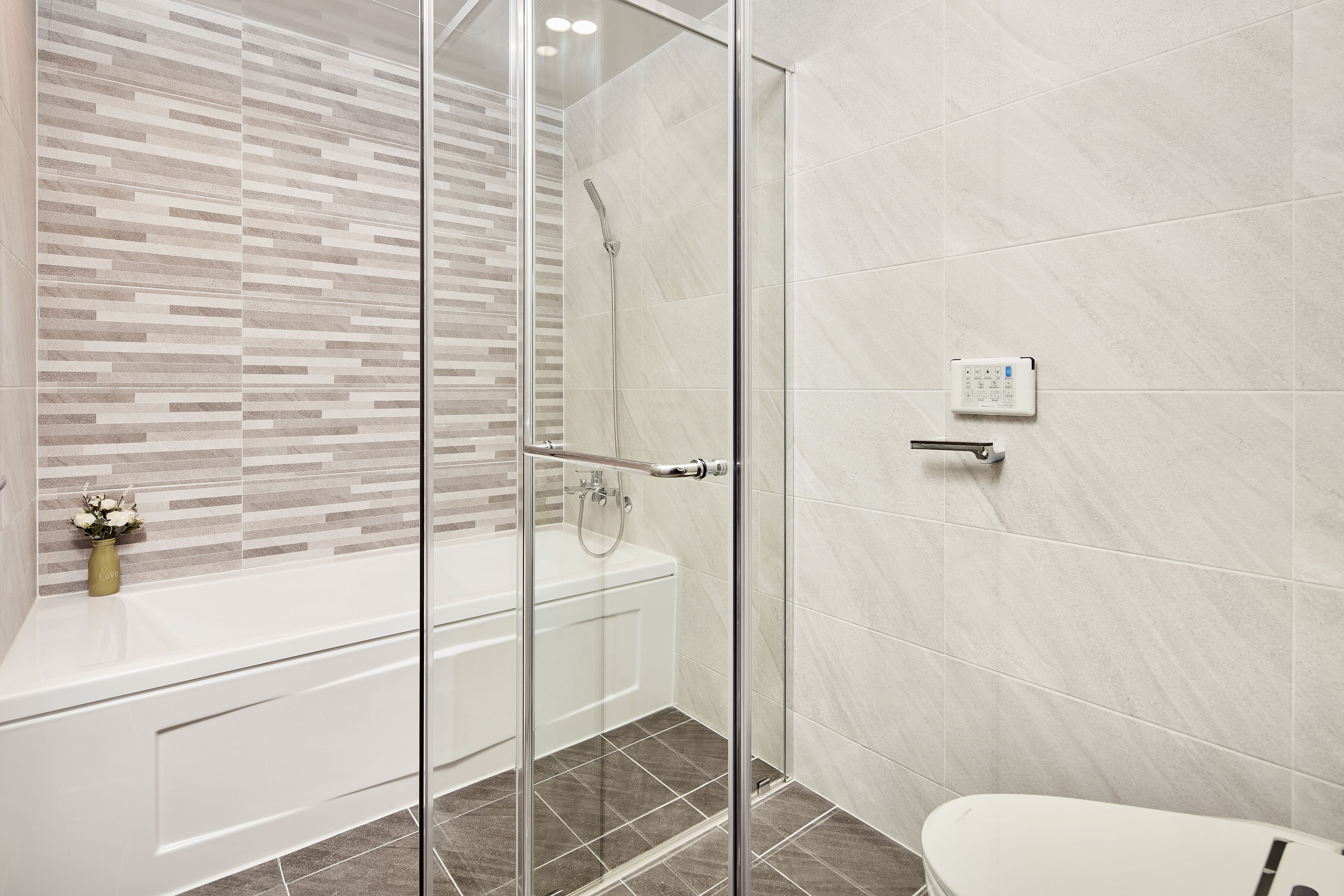 A modern bathroom with a glass shower enclosure, a white bathtub, and a toilet.
